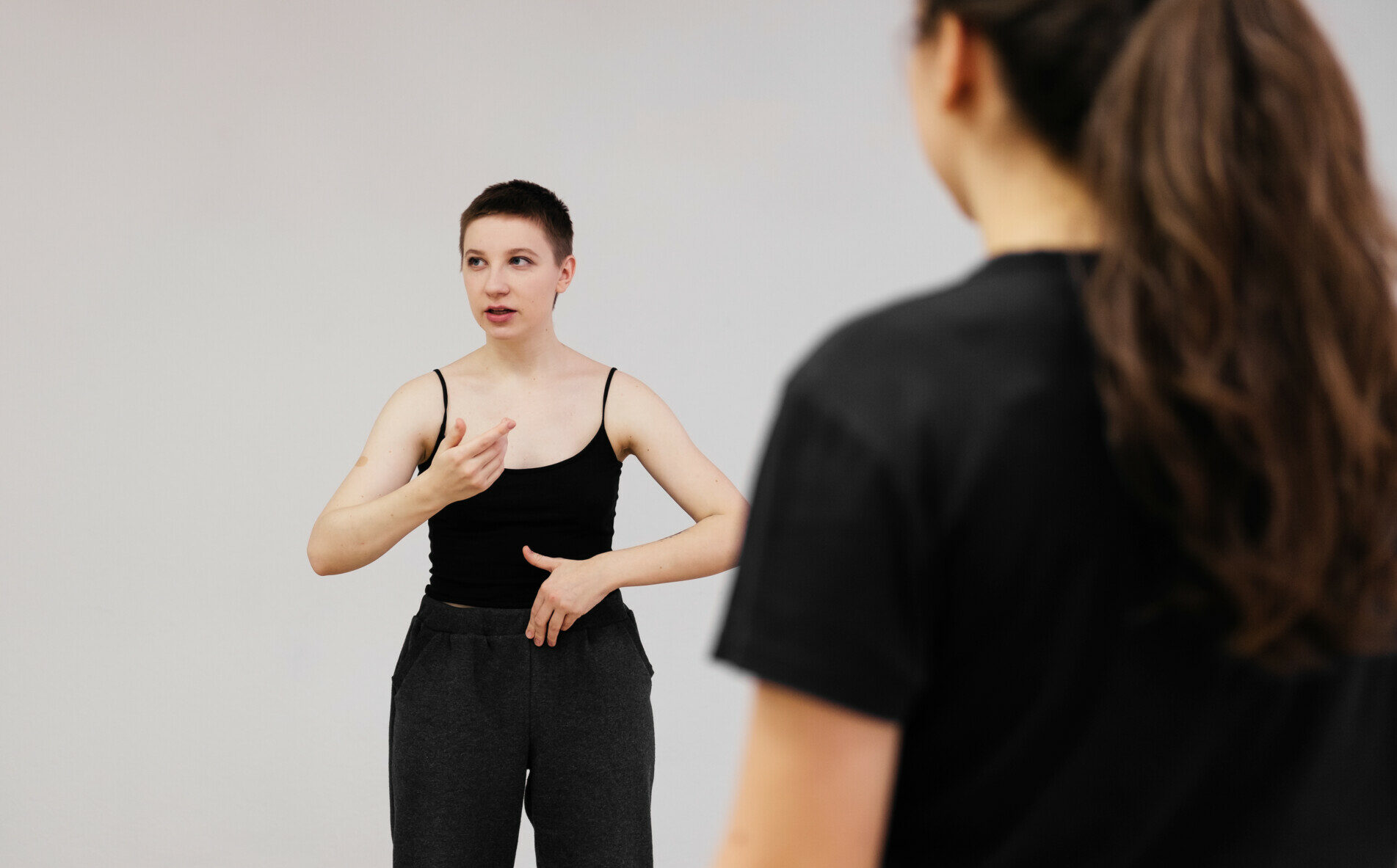 Young speaker woman doing lecture on public. Female actor having a consultation to group of students. Scenic speech exercise. 20 years old coach on stage. Woman with short hair in black top and pants